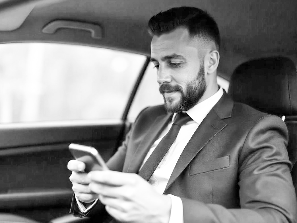 Chaque trajet compte Homme en costume assis dans une voiture, regardant son téléphone.